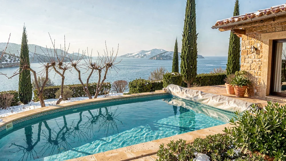 Pool eines Ferienhauses im Winter mit kahlen Weinreben, Zypressen und Blick auf das Meer