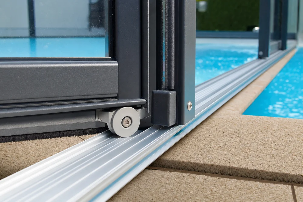 Detailaufnahme der Führungsschiene und Laufrolle einer Poolüberdachung am Beckenrand Detailaufnahme der Führungsschiene und Laufrolle einer Poolüberdachung am Beckenrand