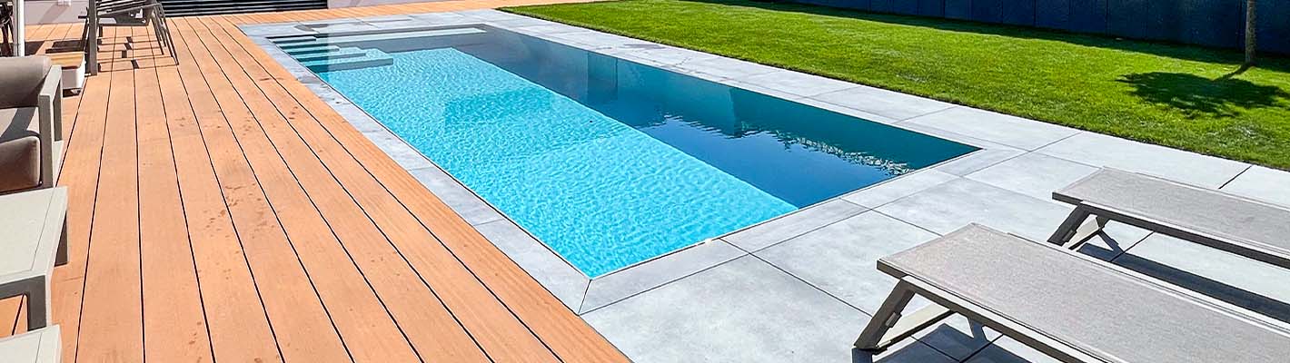 PP Pool Elite – Modernes Gegenstrom-Schwimmbecken im Garten Rechteckiger PP Pool Elite mit eingebauter Gegenstromanlage, umgeben von hellen Betonplatten und einer Holzterrasse, mit Liegen am Beckenrand und grünem Rasen im Hintergrund.