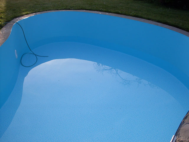 Freiformbecken mit blauer Einhängefolie und integrierter Treppe, teilweise mit Wasser gefüllt