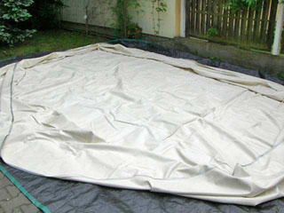 Beige Poolfolie für ein Achtform-Stahlwandbecken, ausgelegt auf einer schwarzen Schutzmatte im Garten.