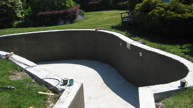 Rohbau eines Freiformbeckens mit Treppe und vorbereiteten Einbauteilen im Garten