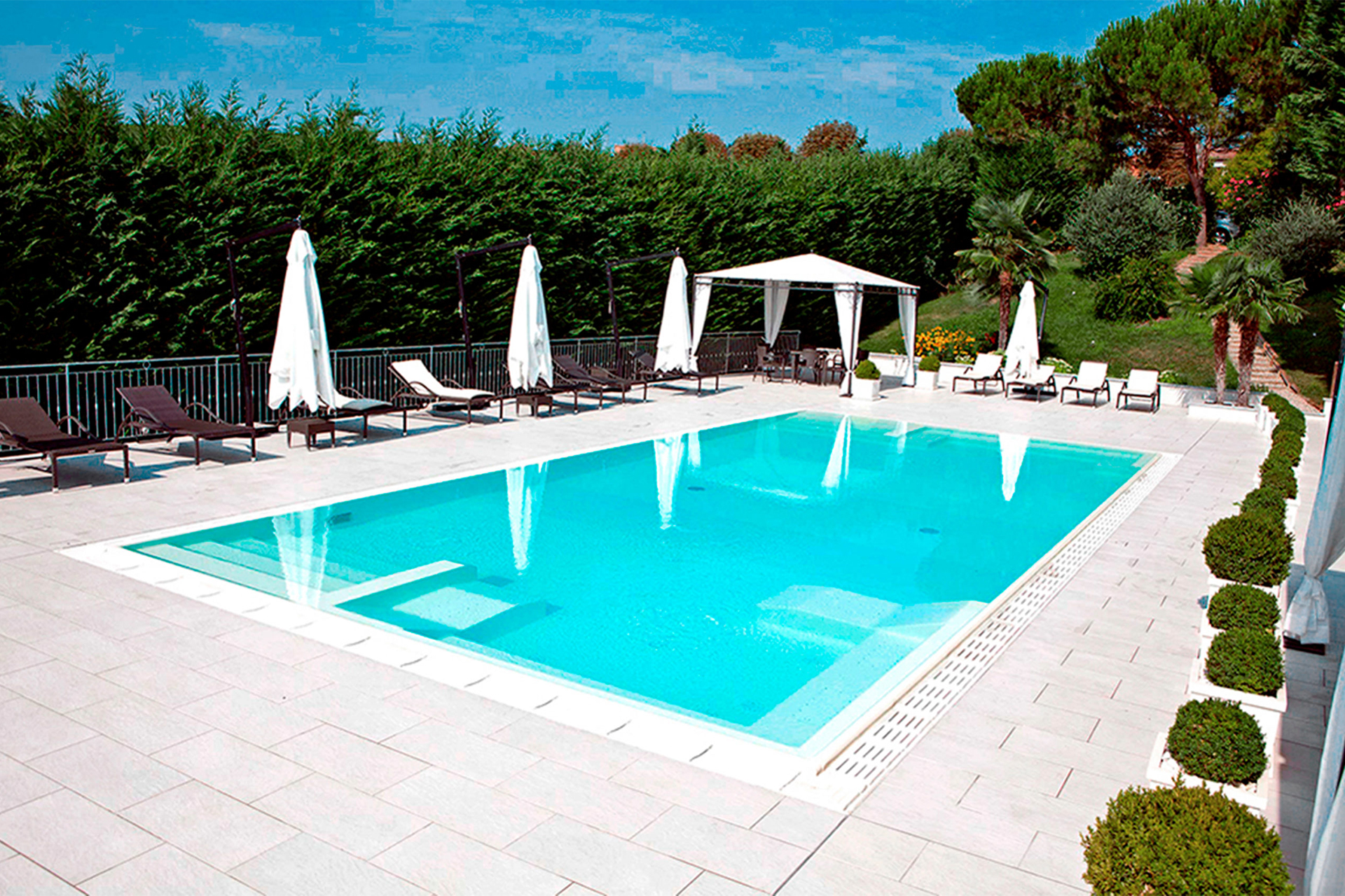 Schwimmbecken mit ELBE ELITE Schwimmbadfolie in Arctic White, umgeben von einer Terrasse mit Liegen und Sonnenschirmen.