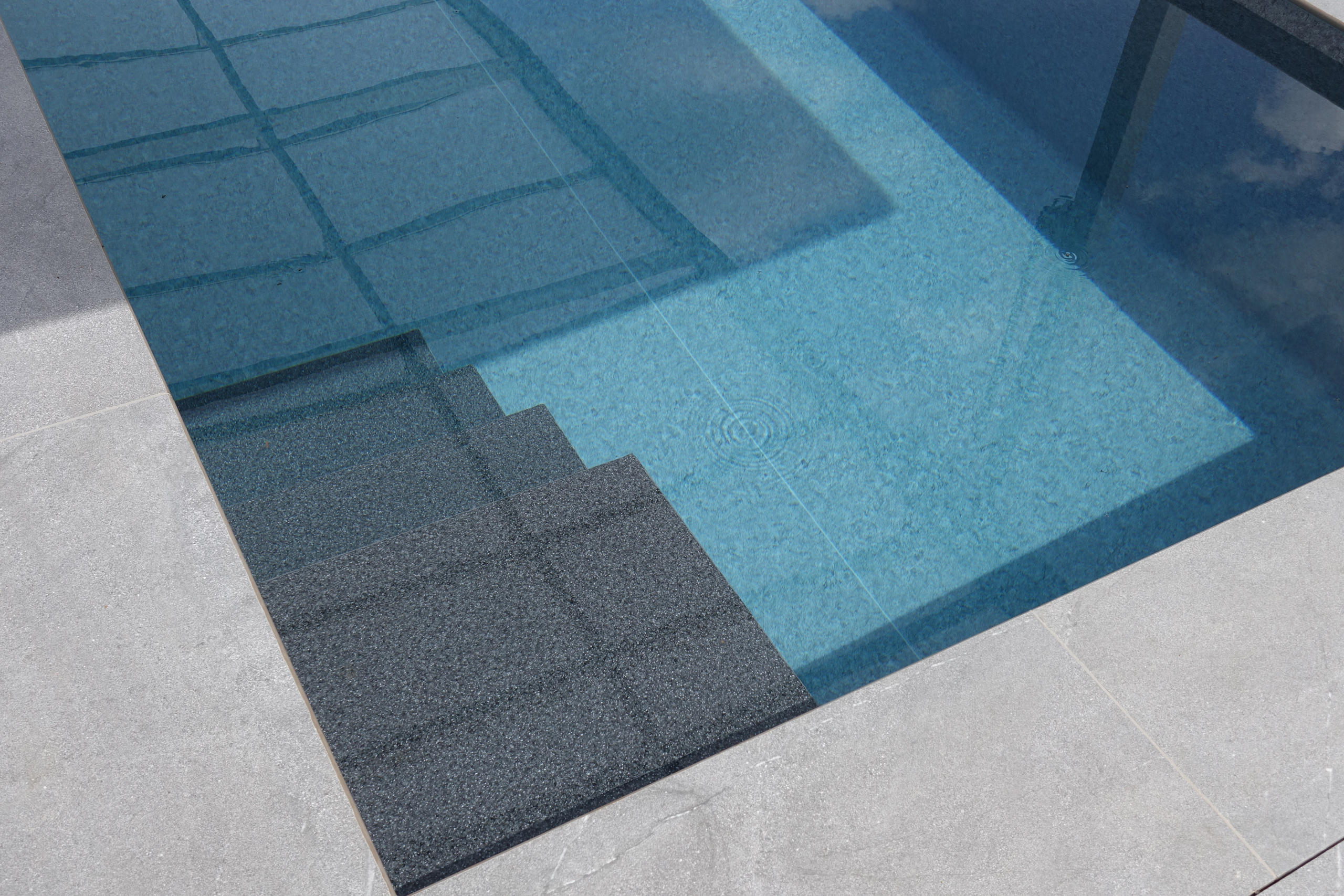 Detailansicht der geraden Treppe mit dunkler Oberfläche im Schwimmbecken, umgeben von hellen Fliesen.