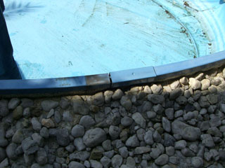 Detailansicht des oberen Beckenrands eines Achtform-Stahlwandbeckens mit blauer Folie und Kiesumrandung.