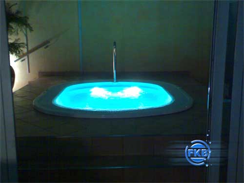 Eingebauter Whirlpool MANDURA mit blauer Unterwasserbeleuchtung und sprudelndem Wasser in einem Raum