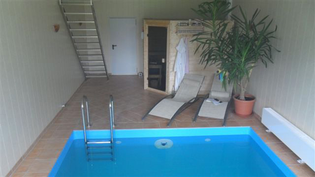 Blick auf ein Hallenbecken mit blauer Einhängefolie, Poolleiter, Sauna und Liegestühlen.