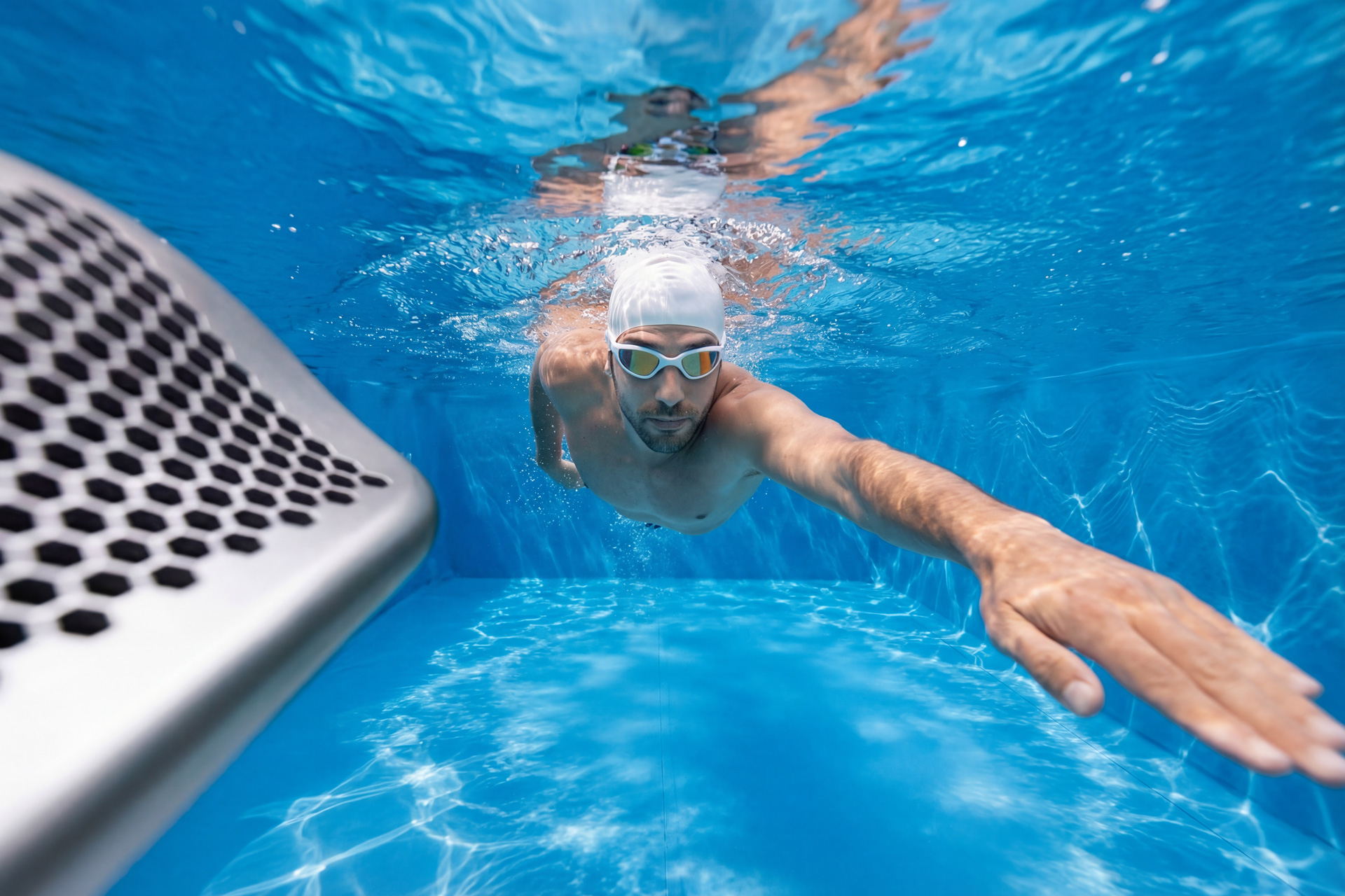 Schwimmer mit Badekappe und Schwimmbrille unter Wasser, im Vordergrund die Aquagem Inverjet Gegenstromanlage