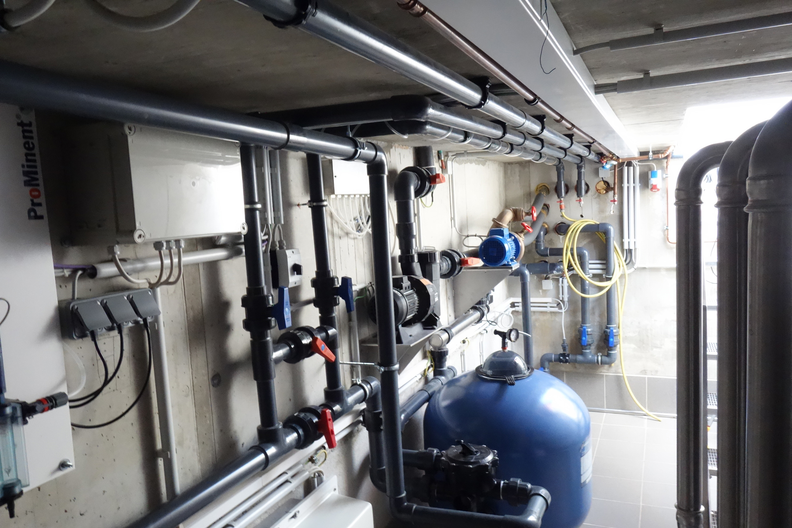 Technikraum mit blauer Filteranlage, Pumpen und grauen PVC-Rohrleitungen für ein Schwimmbecken