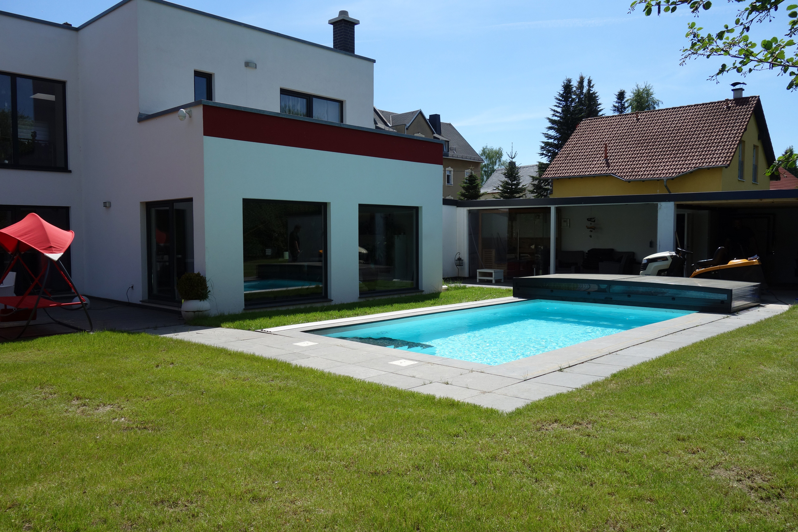Betonbecken mit blauer Wasseroberfläche, grauen Randsteinen und teilweiser Überdachung im Garten