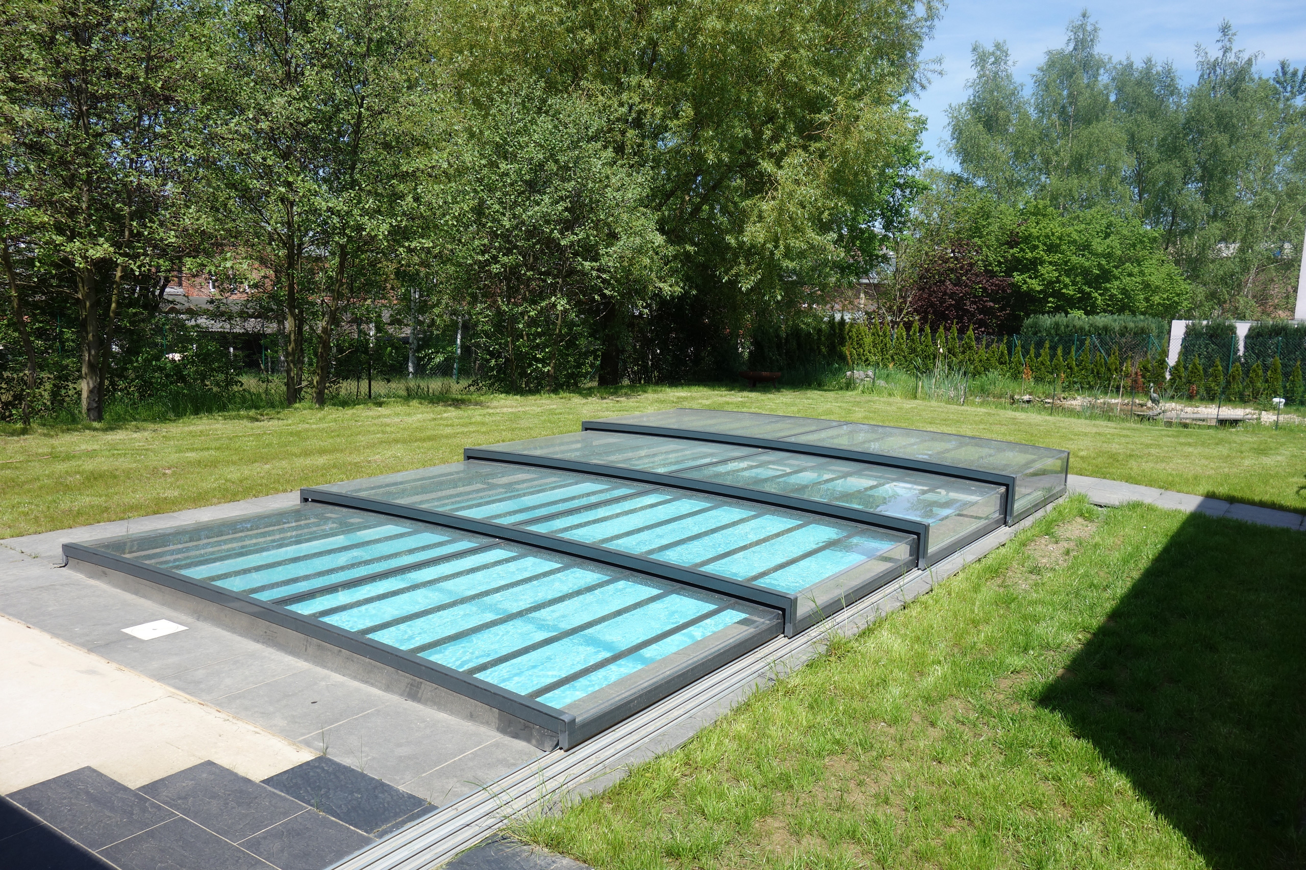 Betonbecken mit Ecktreppe und Podest, abgedeckt mit einer Casablanca Infinity Poolüberdachung im Garten