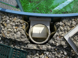 Einbau eines Skimmers in ein Achtform-Stahlwandbecken, umgeben von Kies und Betonbruchstücken.