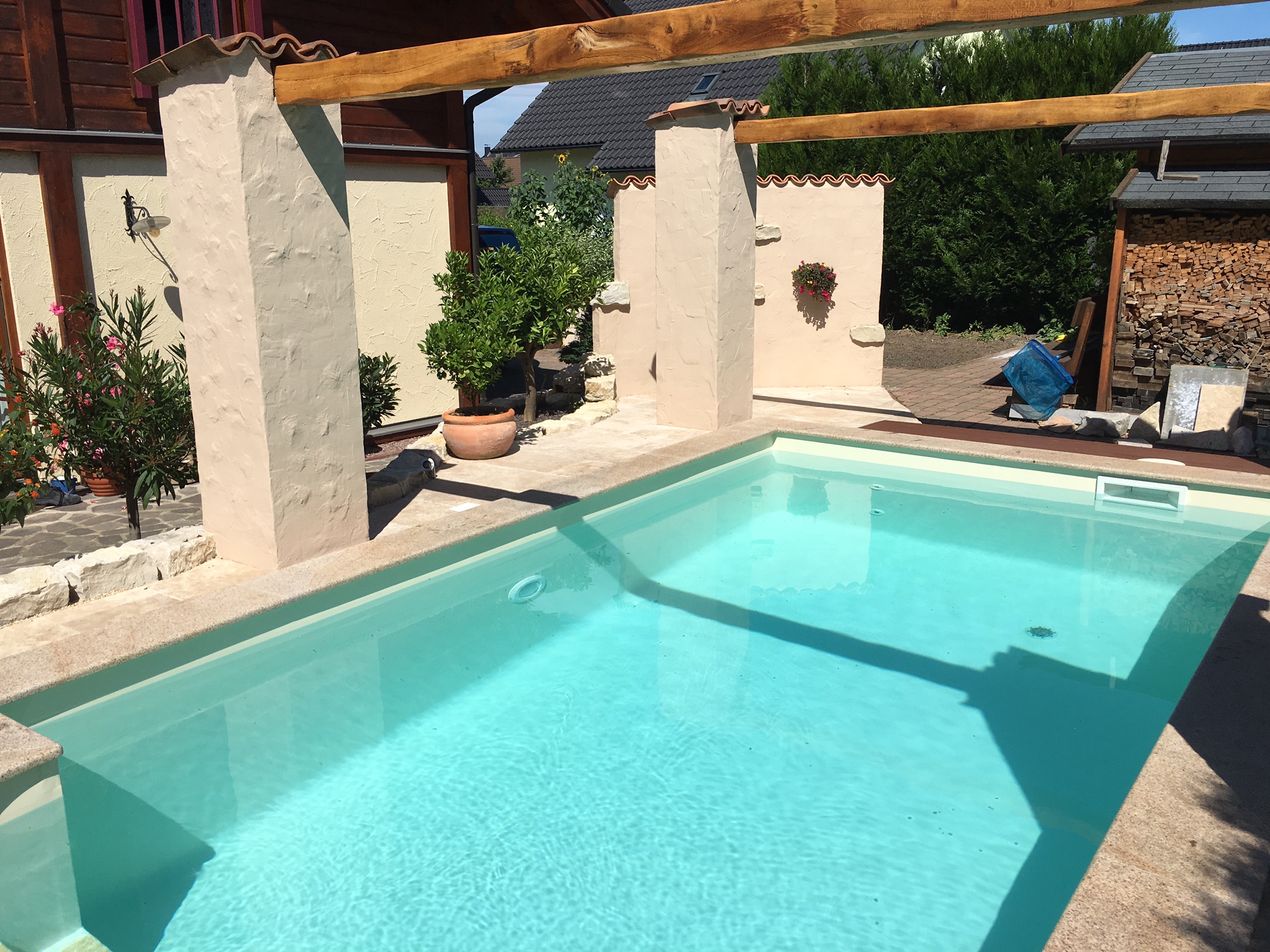 Blick auf das Schwimmbecken mit römischer Treppe, umgeben von einer mediterranen Gestaltung mit Pergola.