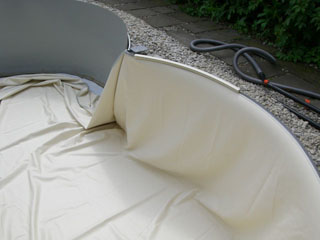 Beige Poolfolie wird in ein Achtform-Stahlwandbecken eingehängt, mit sichtbarer Stahlwand und Kiesumrandung.