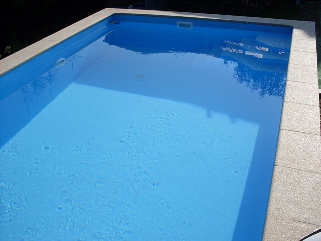 Einbau-Pool mit blauer Folie, Skimmer und Einlaufdüsen, umgeben von hellen Poolrandsteinen