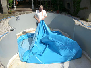 Ein Mann legt eine blaue Poolfolie in ein leeres Achtform-Stahlwandbecken.
