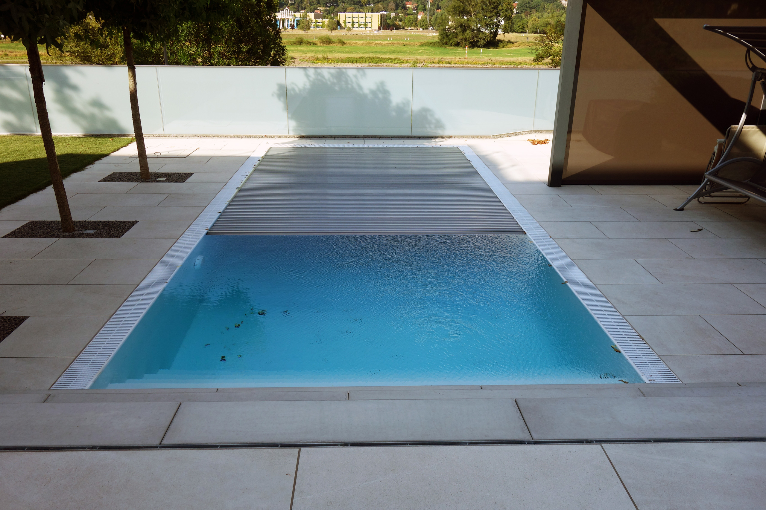 Überlaufpool mit Unterflurrollladen, teilweise geöffnet, um das blaue Wasser und die Überlaufrinne zu zeigen