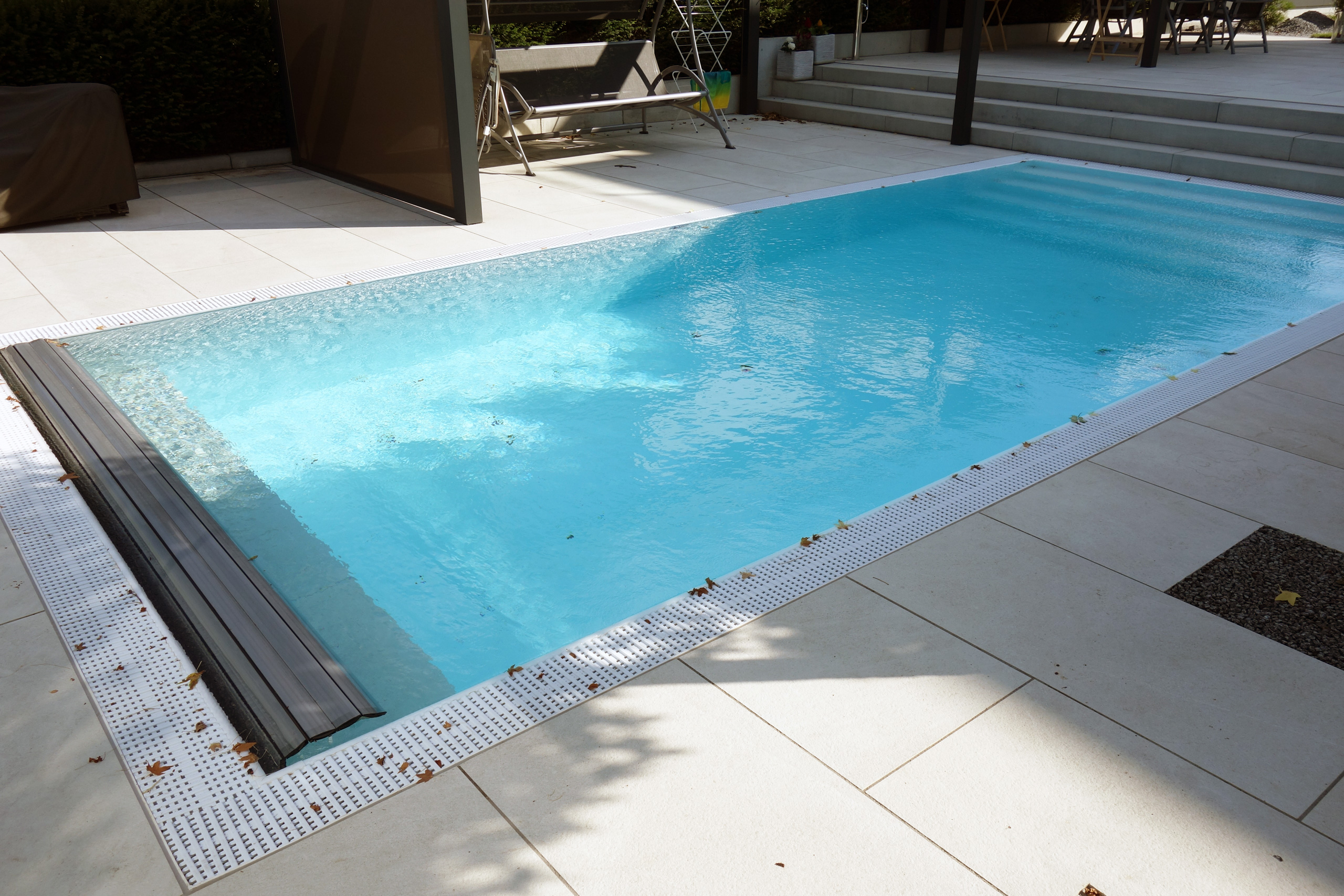 Überlaufpool mit Unterflurrollladen und weißem Überlaufgitter am Beckenrand