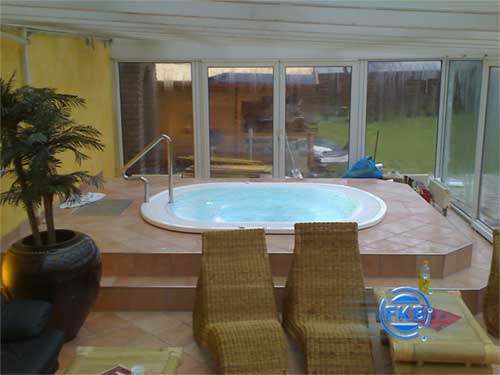 Eingelassener Whirlpool-SPA MANDURA mit Edelstahl-Einstiegshilfe in einem Wintergarten mit Liegen und Pflanzen.